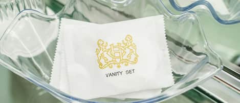 Un bol en verre transparent contenant un tissu blanc orné d’un écusson doré et portant l’inscription « VANITY SET ».