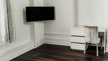 Habitación de esquina con una televisión de pantalla plana montada en la pared, un escritorio blanco con cajones, una silla y piso de madera oscura.