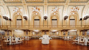 En pragtfuld balsal med detaljerede loftdekorationer, flere lysekroner og et centralt bord med et hvidt lagen.