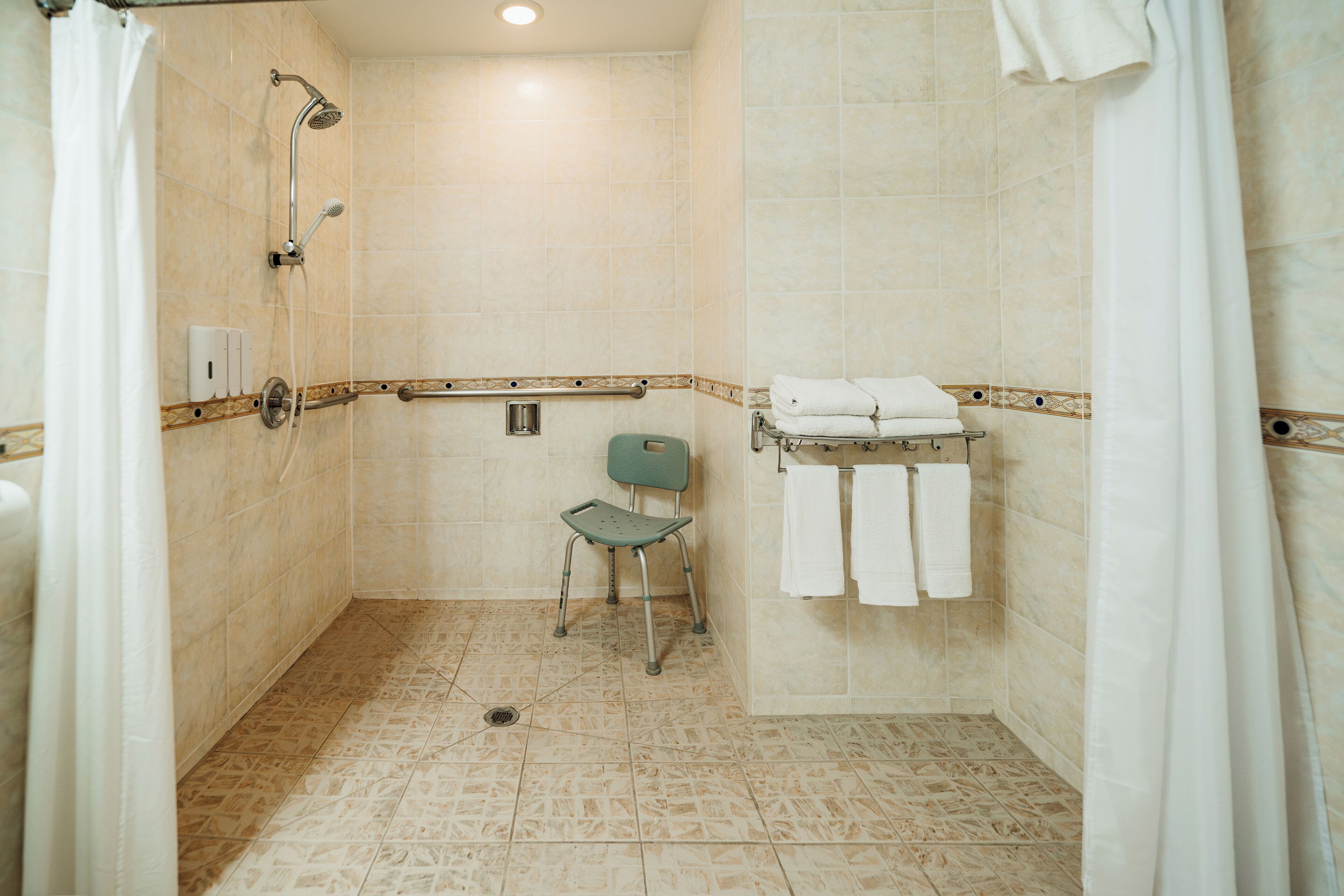 A shower area with a showerhead, a chair, and a towel rack with towels.