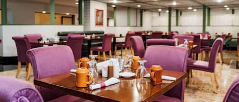 Un comedor con sillas tapizadas de color morado y una mesa de madera preparada para cuatro personas.