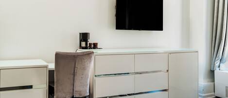 A modern hotel room with a bed, a desk with a chair, a flat-screen TV, and a coffee maker.