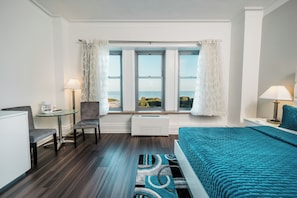 A hotel room with a bed, a desk, a chair, a window with curtains, and a view of the outdoors.