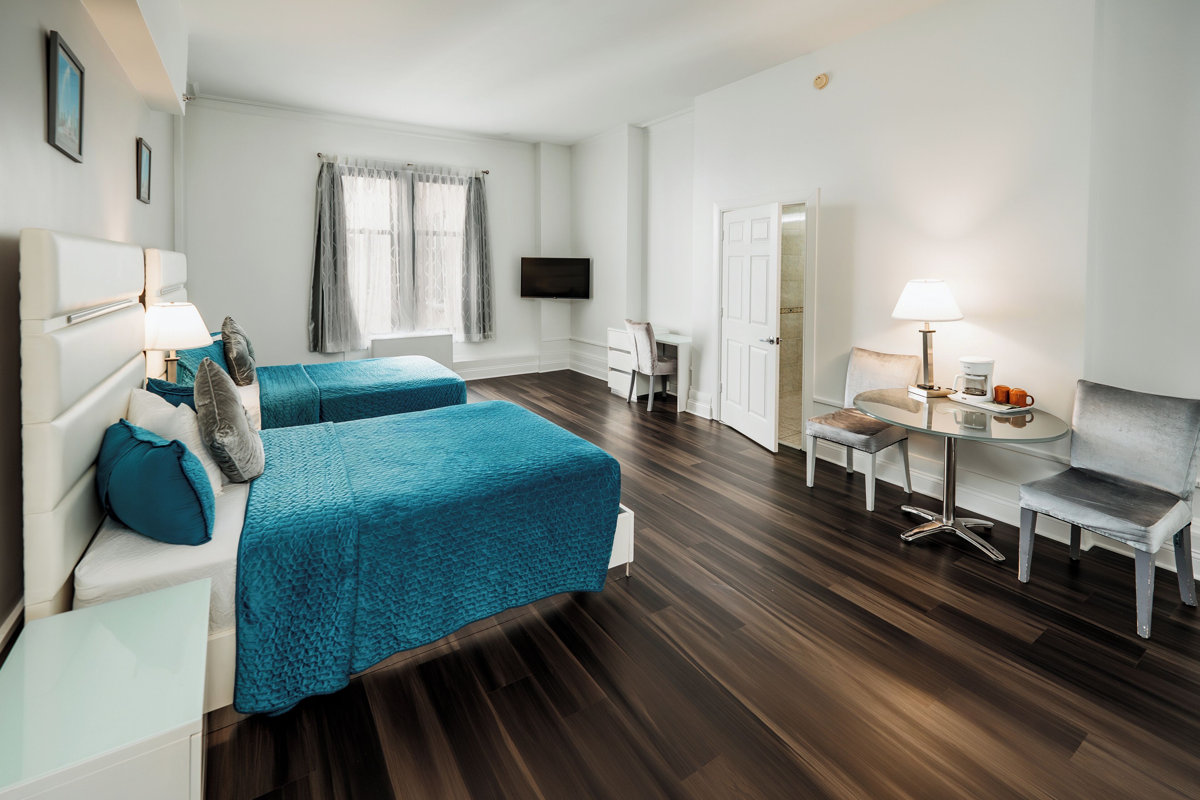 Une chambre d’hôtel avec deux lits, un bureau, une chaise, une télévision et une fenêtre avec des rideaux.