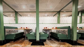 Ein Restaurantinneres mit grünen Sitzecken, Marmorböden, gemustertem Wandpapier und Deckenleuchten.
