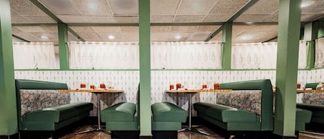 Ein Restaurantinneres mit grünen Sitzecken, Marmorböden, gemustertem Wandpapier und Deckenleuchten.