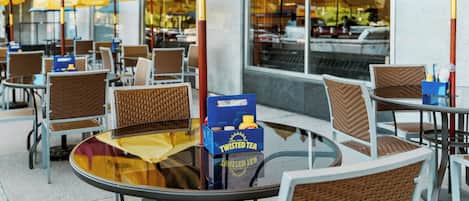 Un área de estar con sombrillas amarillas, sillas de mimbre y una mesa de vidrio con una caja de Twisted Tea.