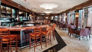 En rummelig bar med en central bardisk, flere siddepladser inklusive barstole og borde, samt et godt oplyst loft med indbygningsbelysning.