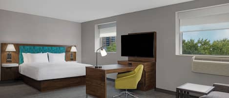 Quarto de hotel com cama, escrivaninha, cadeira, televisão e janela com vista.