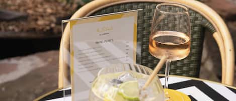 Un panel de menú con el título 'SMALL PLATES' que muestra varios platos y sus precios, una copa de vino blanco y un mantel a rayas.
