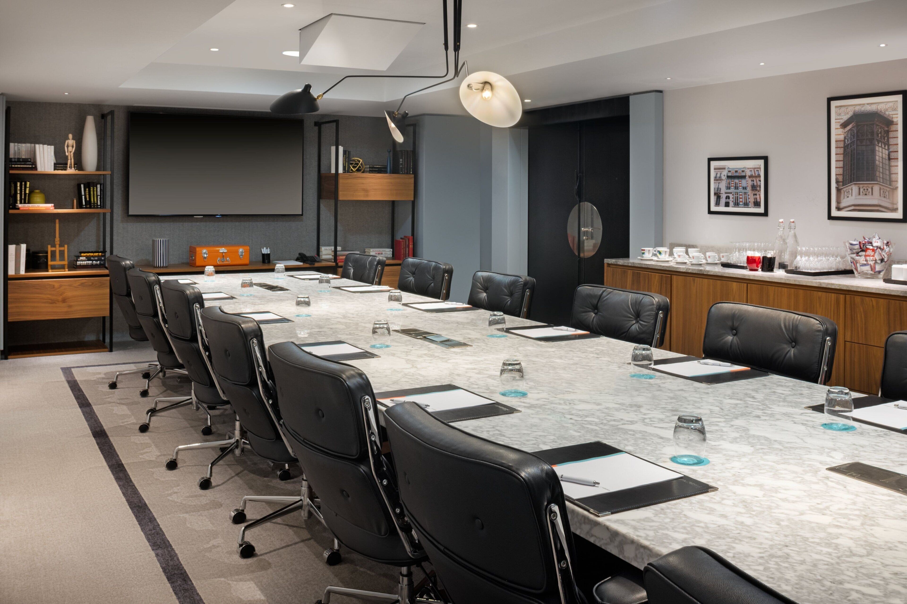 A conference room with a long table, black leather chairs, a projector screen, and a coffee station.