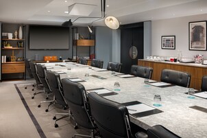 A conference room with a long table, black leather chairs, a projector screen, and a coffee station.