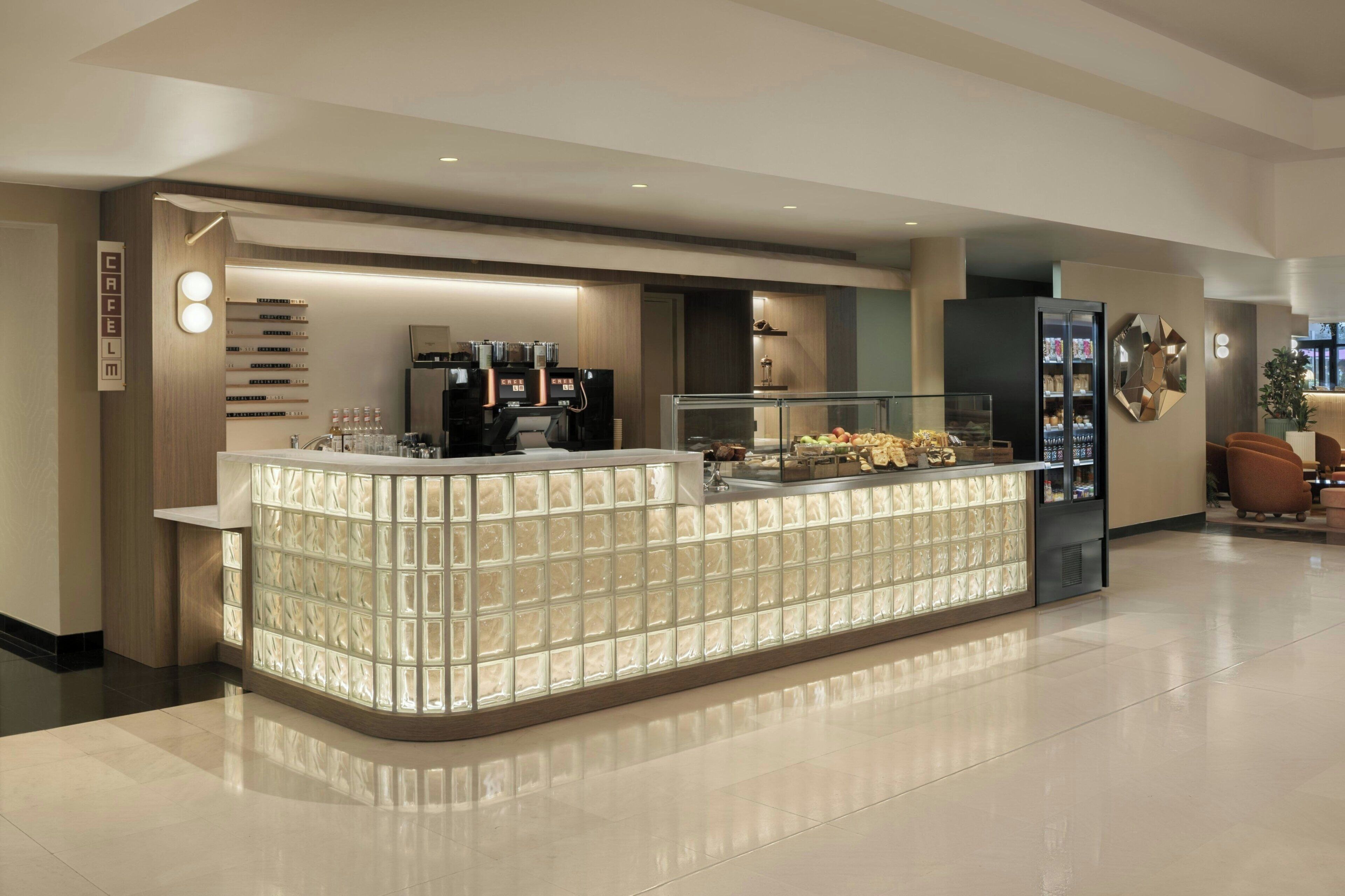A modern reception area with a glass partition, a coffee machine, and a display case with snacks.