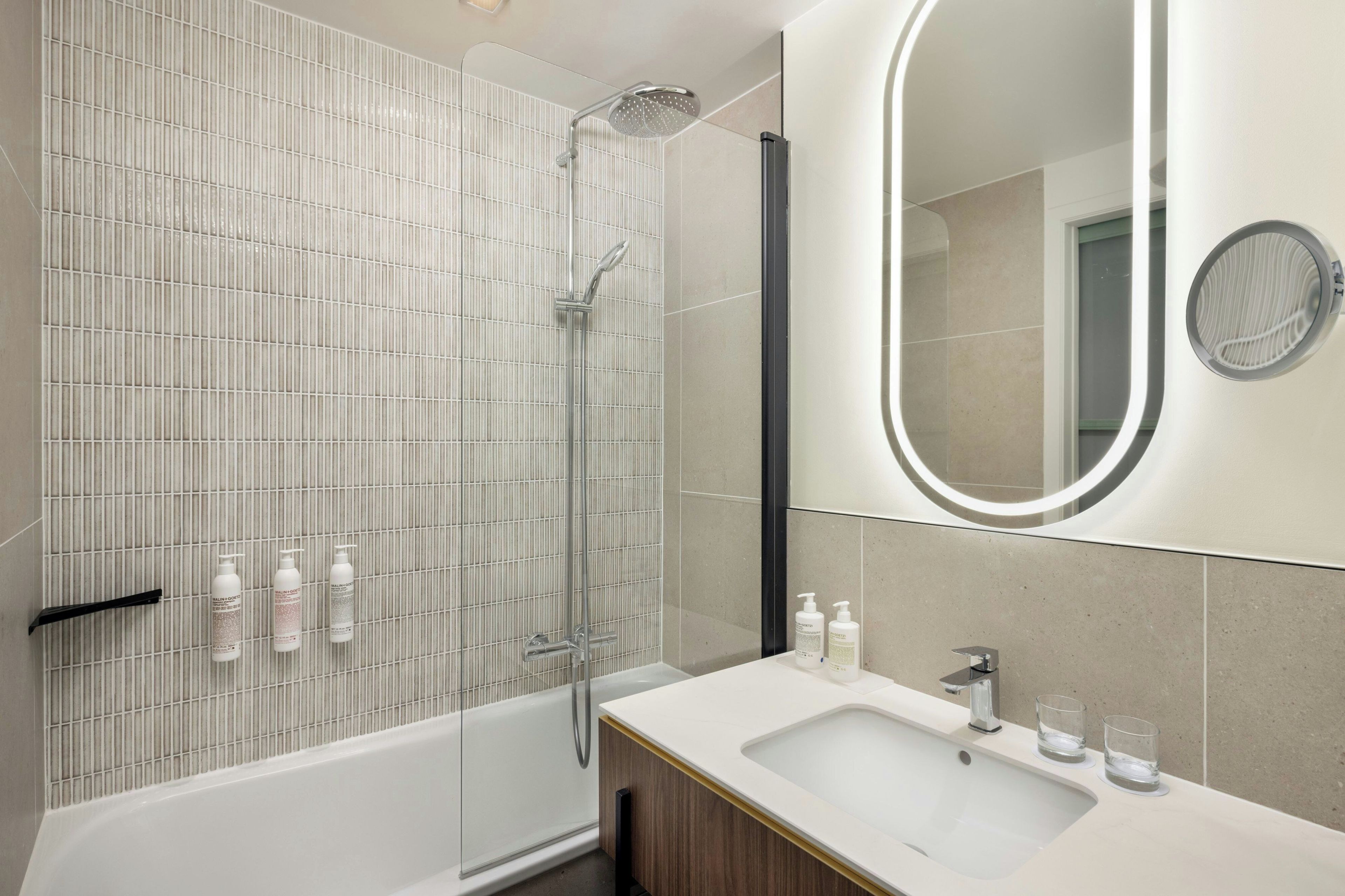 Une salle de bain moderne équipée d’une douche, d’un grand miroir et d’un lavabo avec des articles de toilette.
