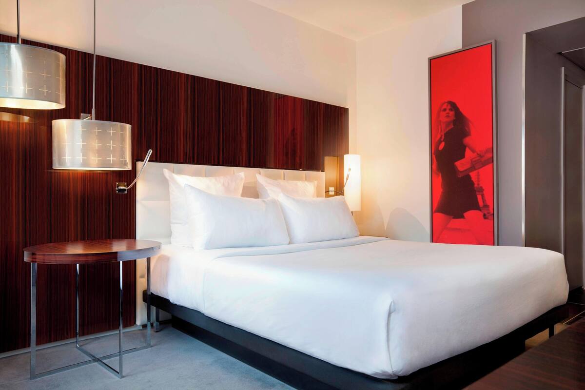 Una habitación de hotel moderna con una cama grande, una mesita auxiliar pequeña y una pared decorativa de madera.