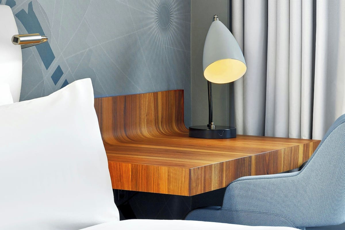 A hotel room with a bed, a nightstand, a lamp, a chair, and a curtain.