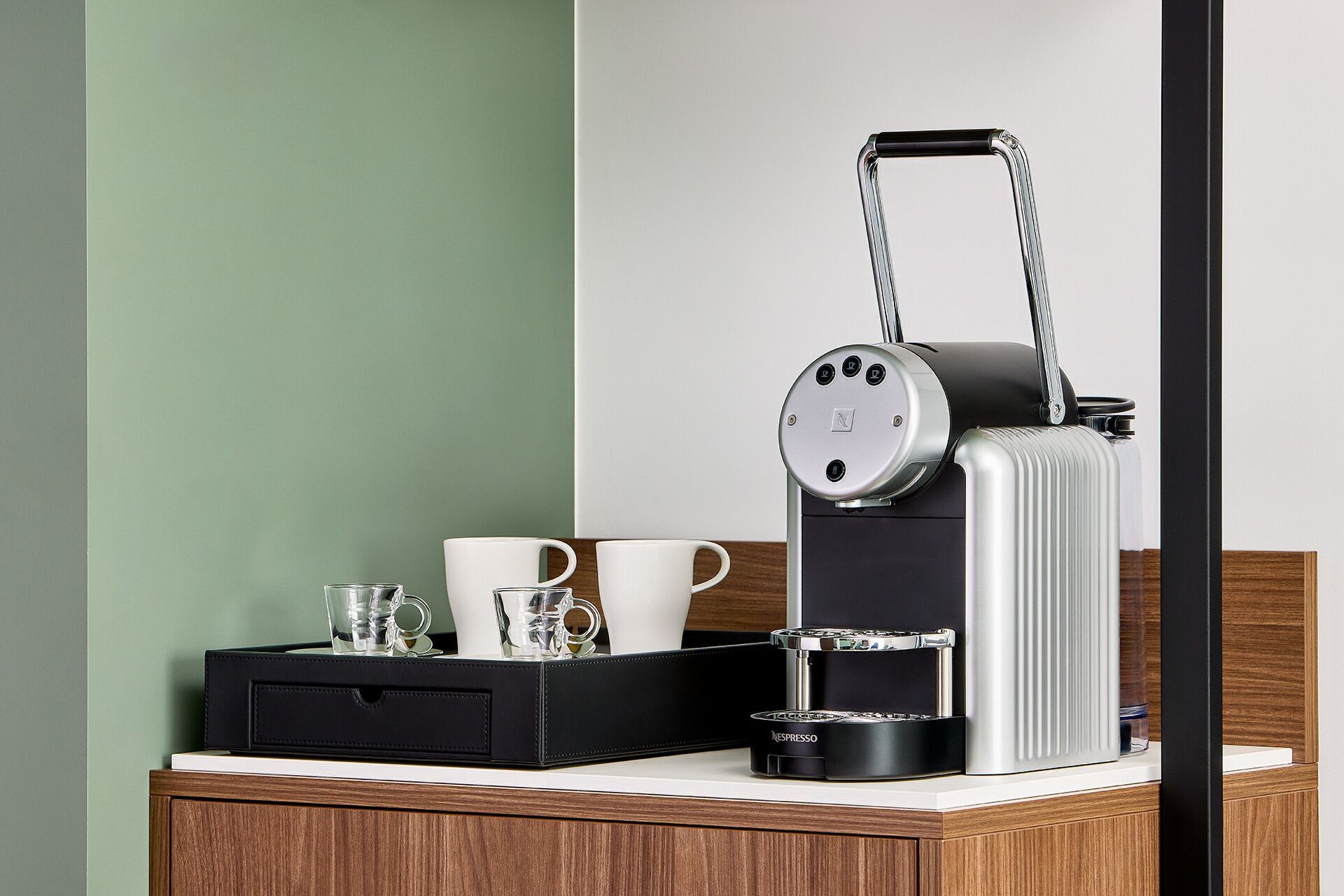 A coffee maker with a handle, a black carrying case, and two white cups on a wooden surface.