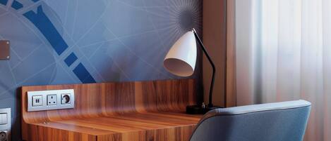 A modern hotel room with a wooden desk, a lamp, and a power outlet.