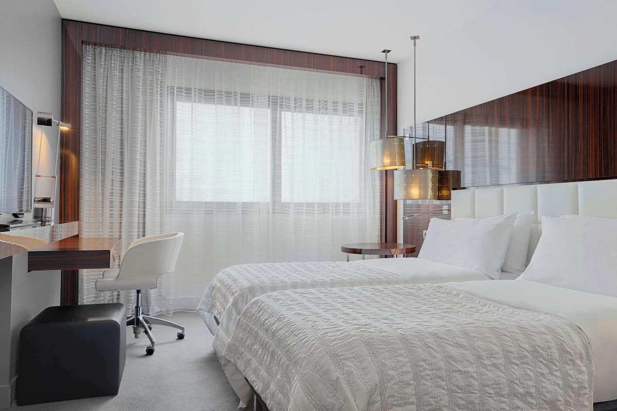 A hotel room with a large bed, a desk, a chair, and a lamp.