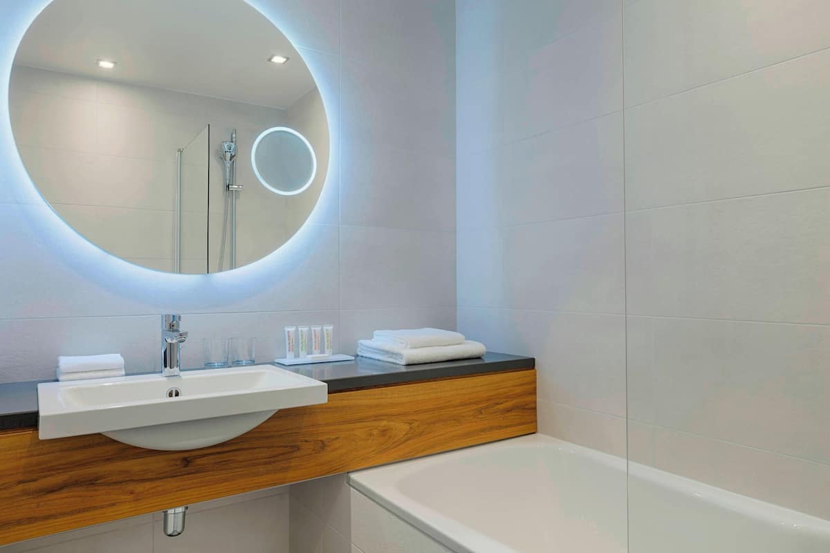 A modern bathroom with a round mirror, white sink, and bathtub.