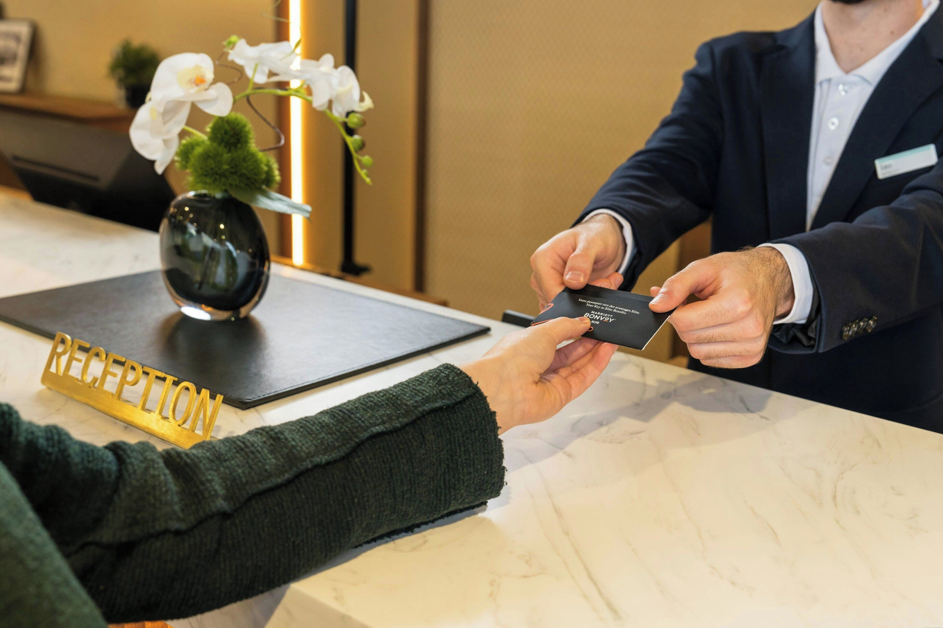 Un comptoir d’accueil avec une pancarte indiquant « RÉCEPTION », une tablette noire et une personne qui tend une carte.