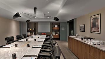 A conference room with a long table, black leather chairs, a wooden counter with cups and saucers, and framed pictures on the wall.