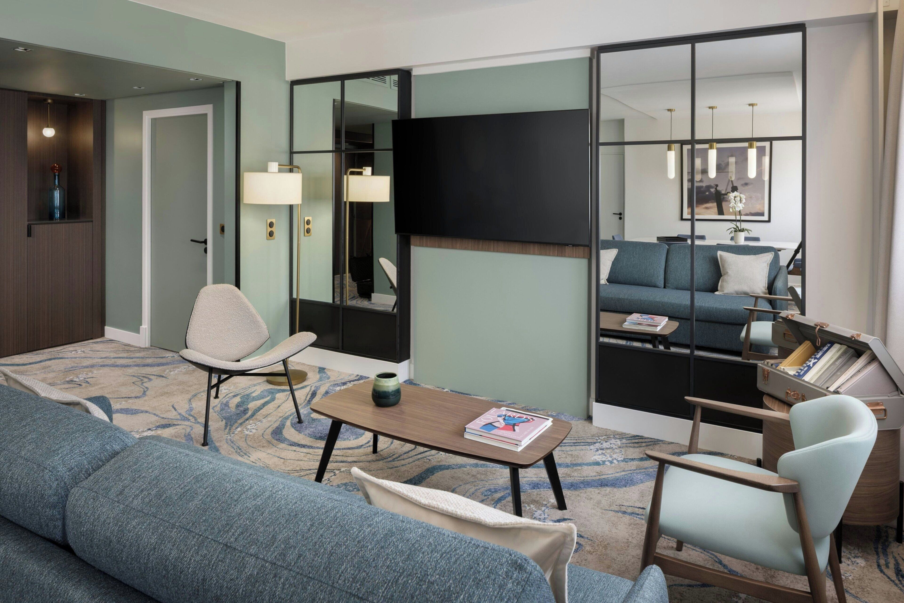 Un salon moderne comprenant un canapé, des fauteuils, une table basse et un téléviseur à écran plat fixé au mur.