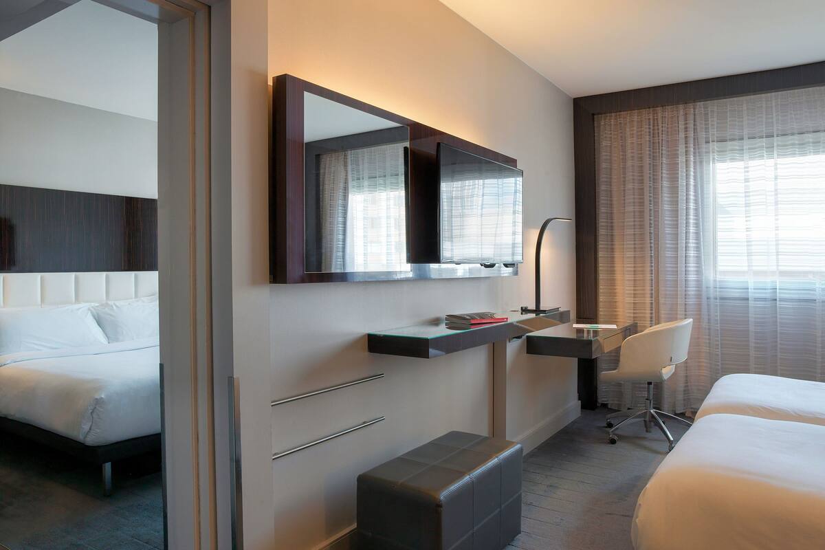 Una habitación de hotel moderna con una cama grande, un escritorio con una silla, un espejo y una ventana con cortinas.