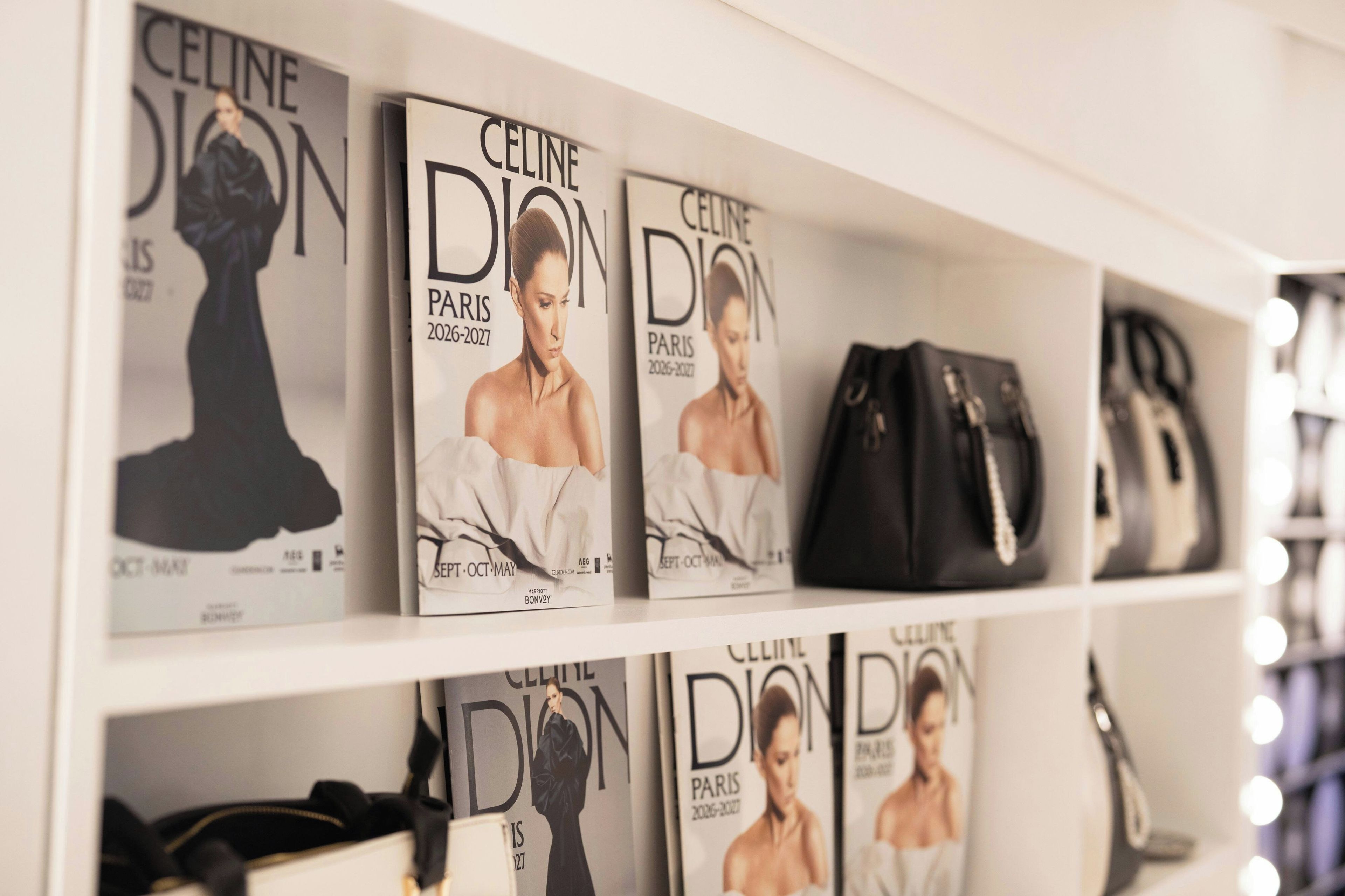 A shelf with multiple copies of 'Celine Dion' magazine, a black handbag, and a pair of black shoes.