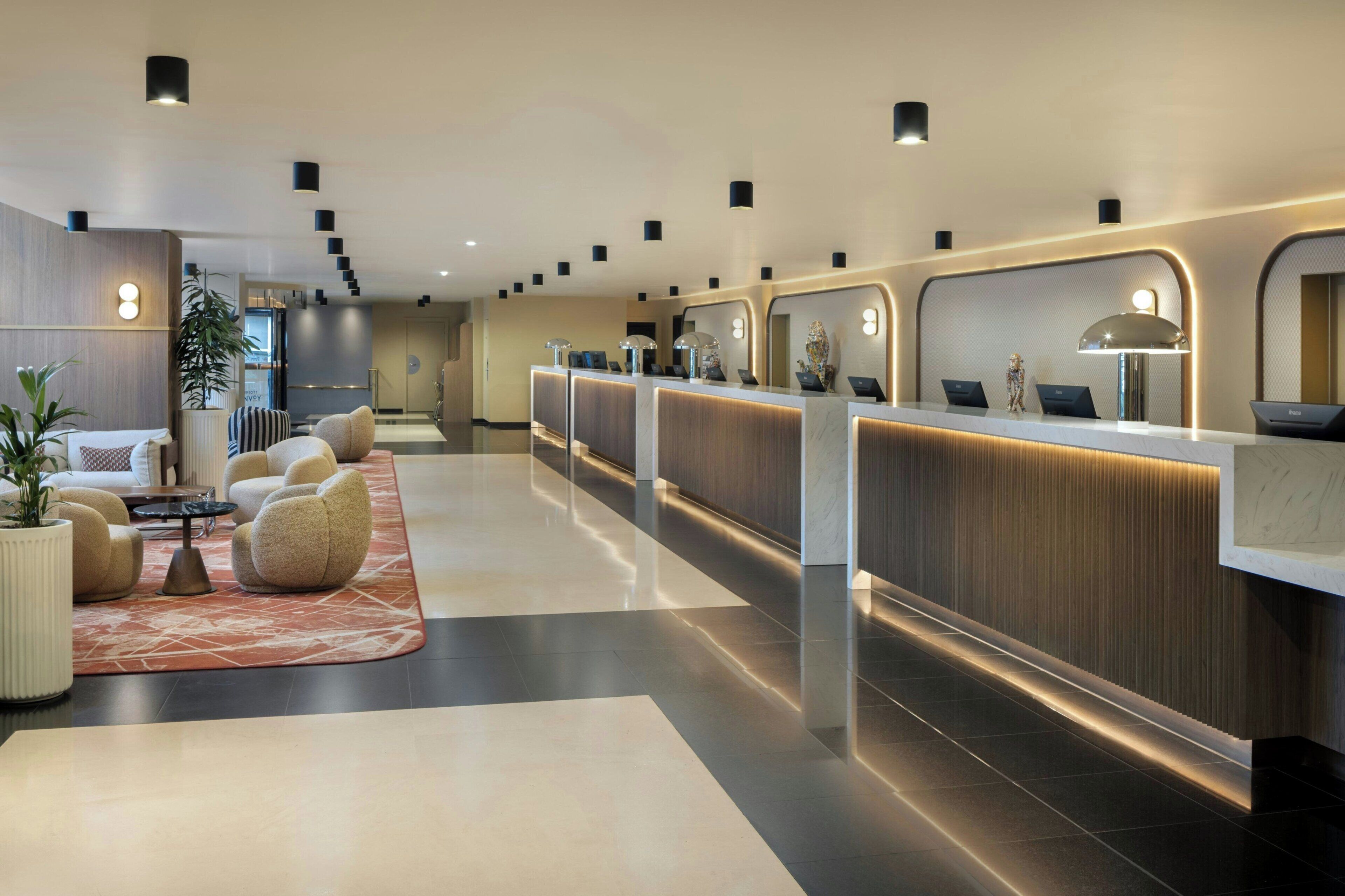 Un hall d’hôtel moderne avec un comptoir d’accueil, un espace salon et une plante.