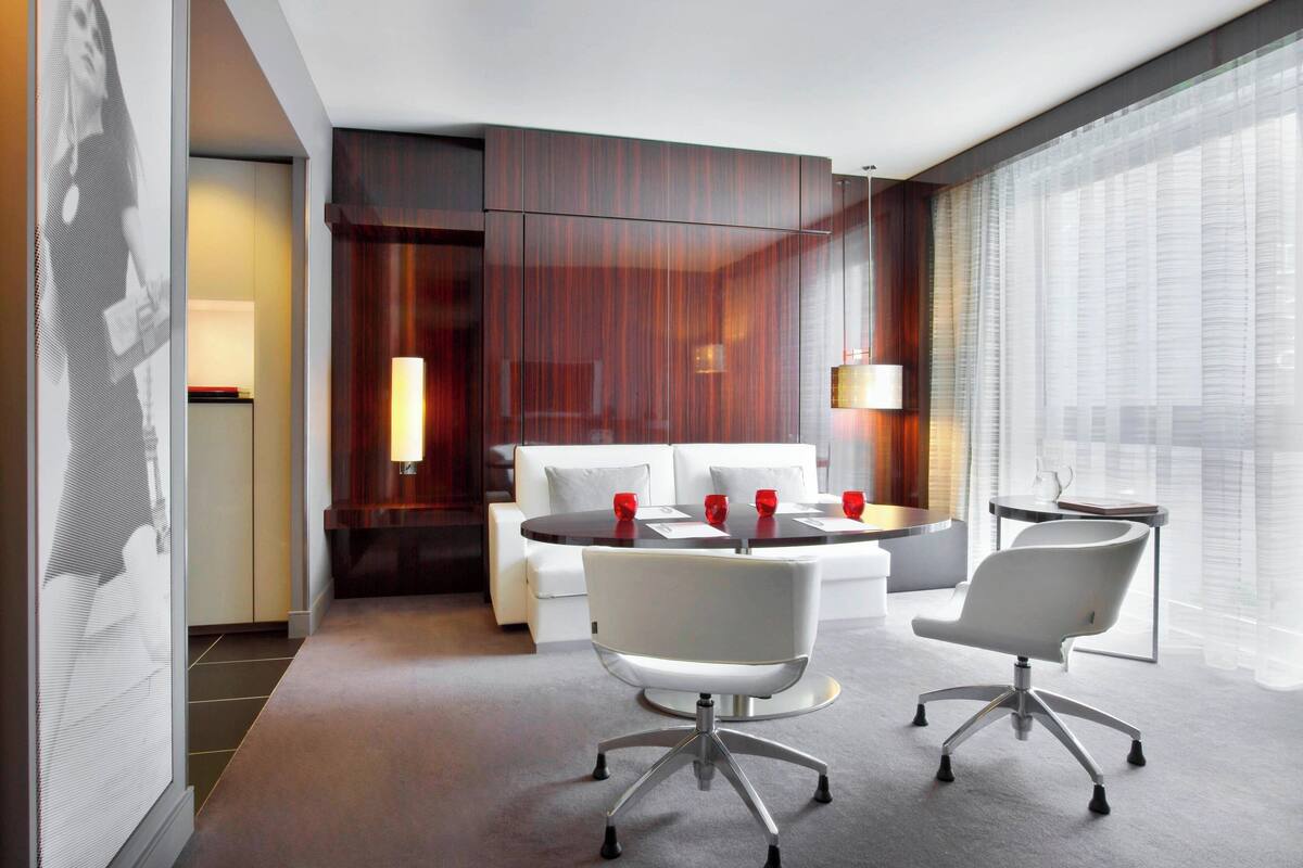 Una habitación de hotel moderna con sofá, dos sillones, una mesa redonda y una mesita auxiliar.