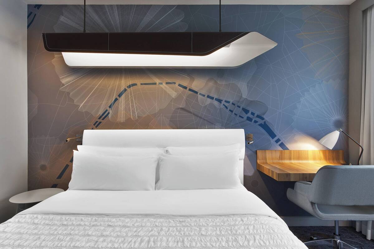Una habitación de hotel moderna con una cama grande, un escritorio y una pared con un diseño geométrico.