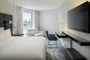 A hotel room with a large bed, a desk with a flat-screen TV, a seating area with a chair, and a view of the cityscape through the window. - Le Méridien Paris Arc De Triomphe (Paris)