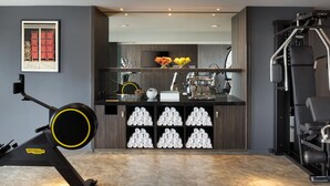 A gym with exercise equipment, a wall-mounted TV, and a shelf with towels and a vase. - Le Méridien Paris Arc De Triomphe (Paris)
