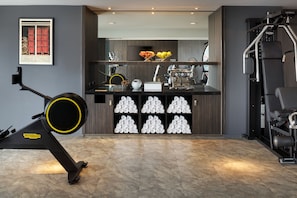 A gym with exercise equipment, a wall-mounted TV, and a shelf with towels and a vase. - Le Méridien Paris Arc De Triomphe (Paris)