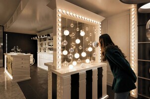 Una stanza con uno specchio da trucco illuminato, un comò bianco e una mensola con oggetti decorativi.