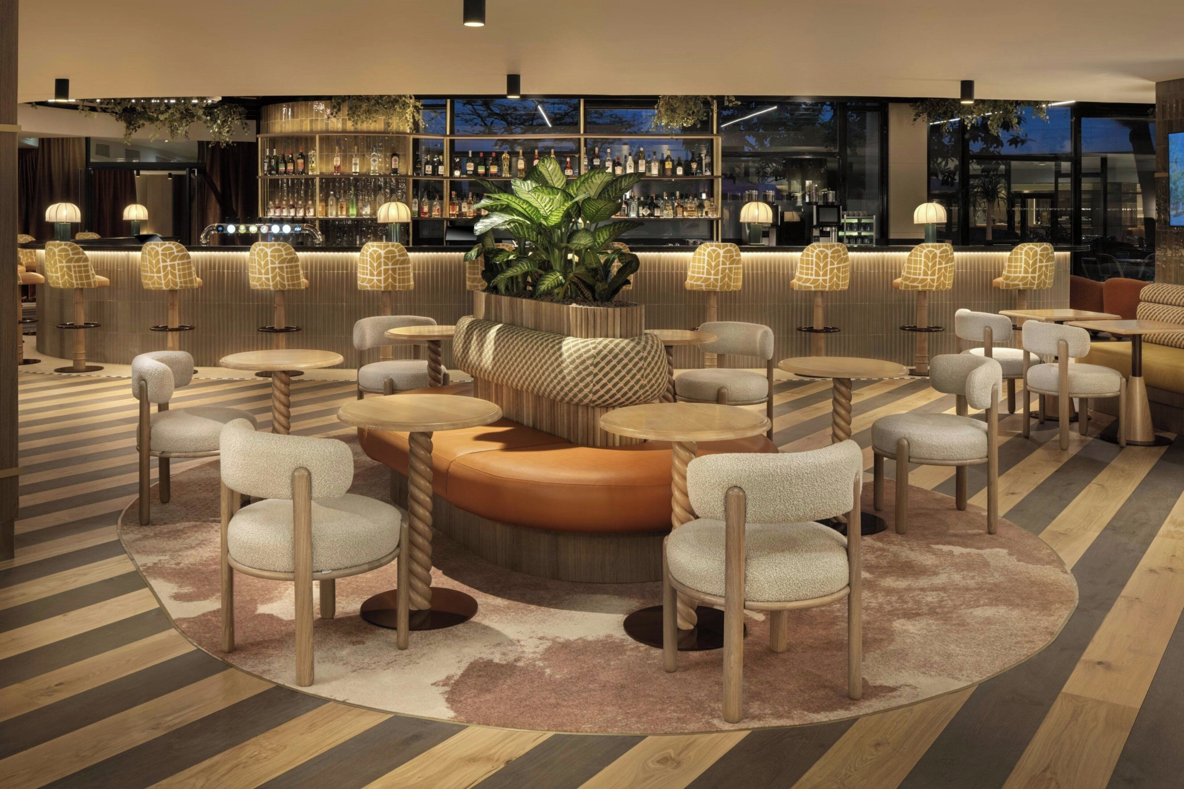 Zona de bar moderna con mesas redondas, asientos acolchados y una variedad de botellas de licor en estanterías.
