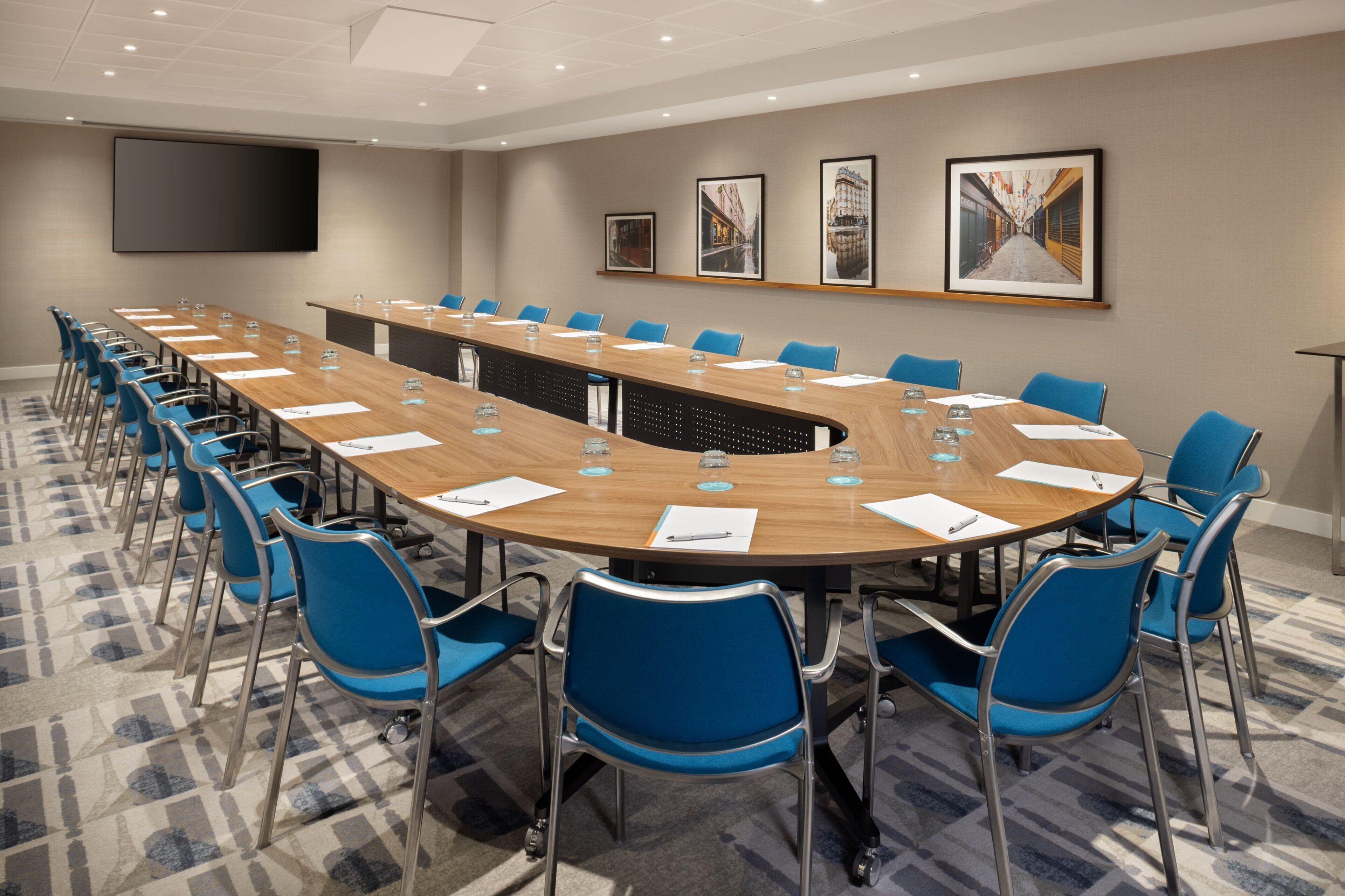 A conference room with a long table, blue chairs, and a large screen on the wall.