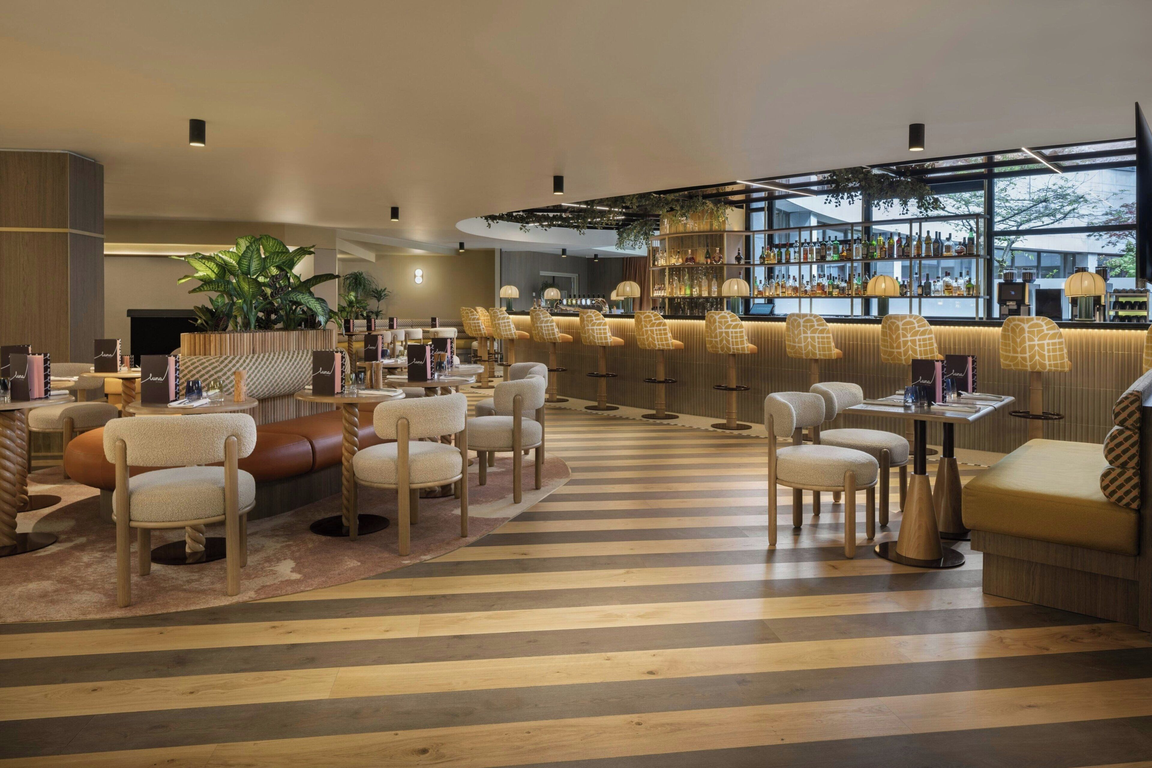 A modern bar area with striped flooring, multiple seating options including sofas and chairs, and a large window with a view.