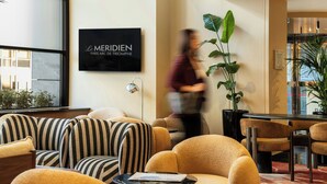 A hotel lobby with striped sofas, a black sign, and a large plant. - Le Méridien Paris Arc De Triomphe (Paris)