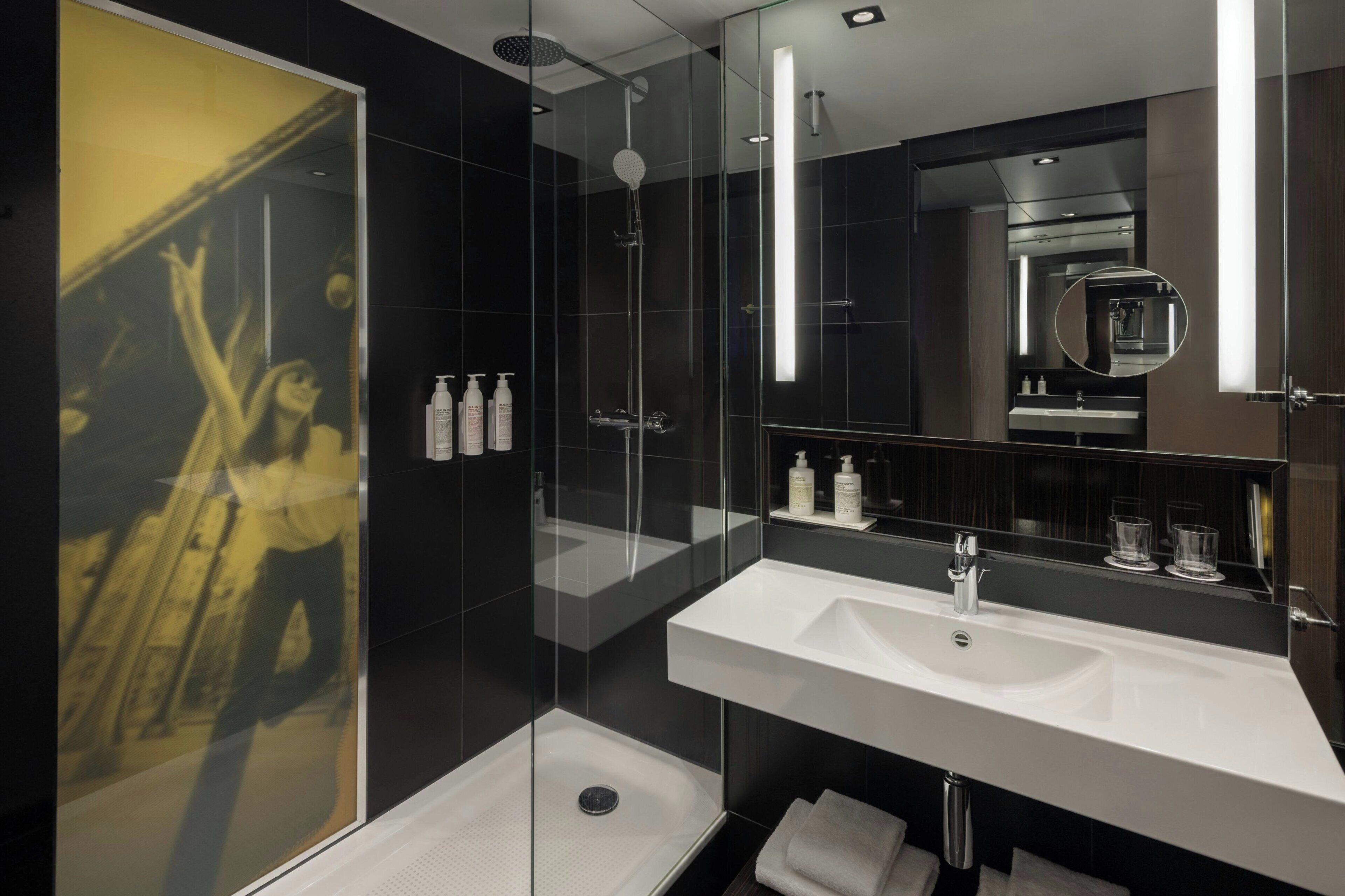 A modern bathroom with a glass shower enclosure, a large mirror, and two sinks.