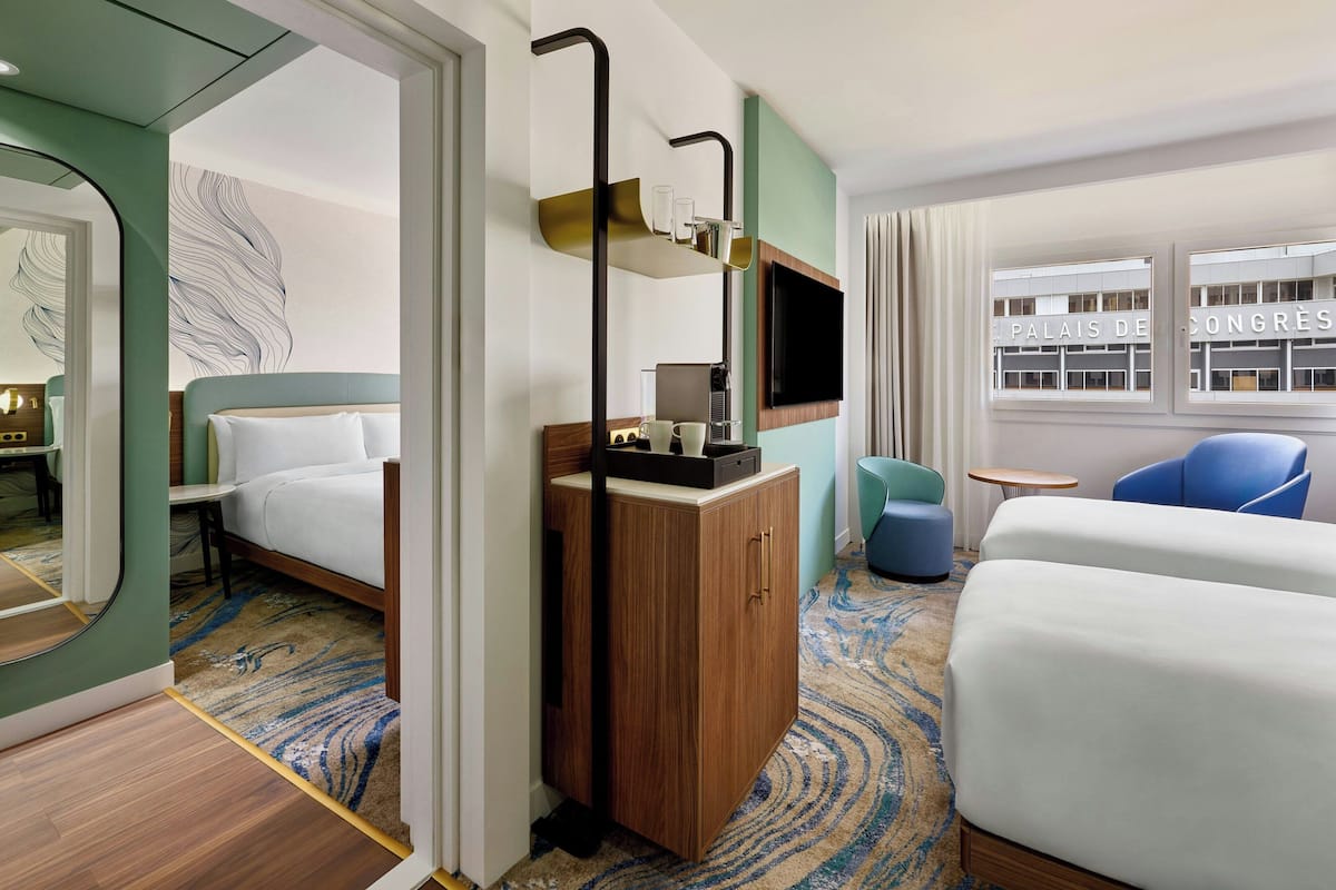 A hotel room with a bed, a wooden cabinet, a TV, and a view of the Palais de Congrès.