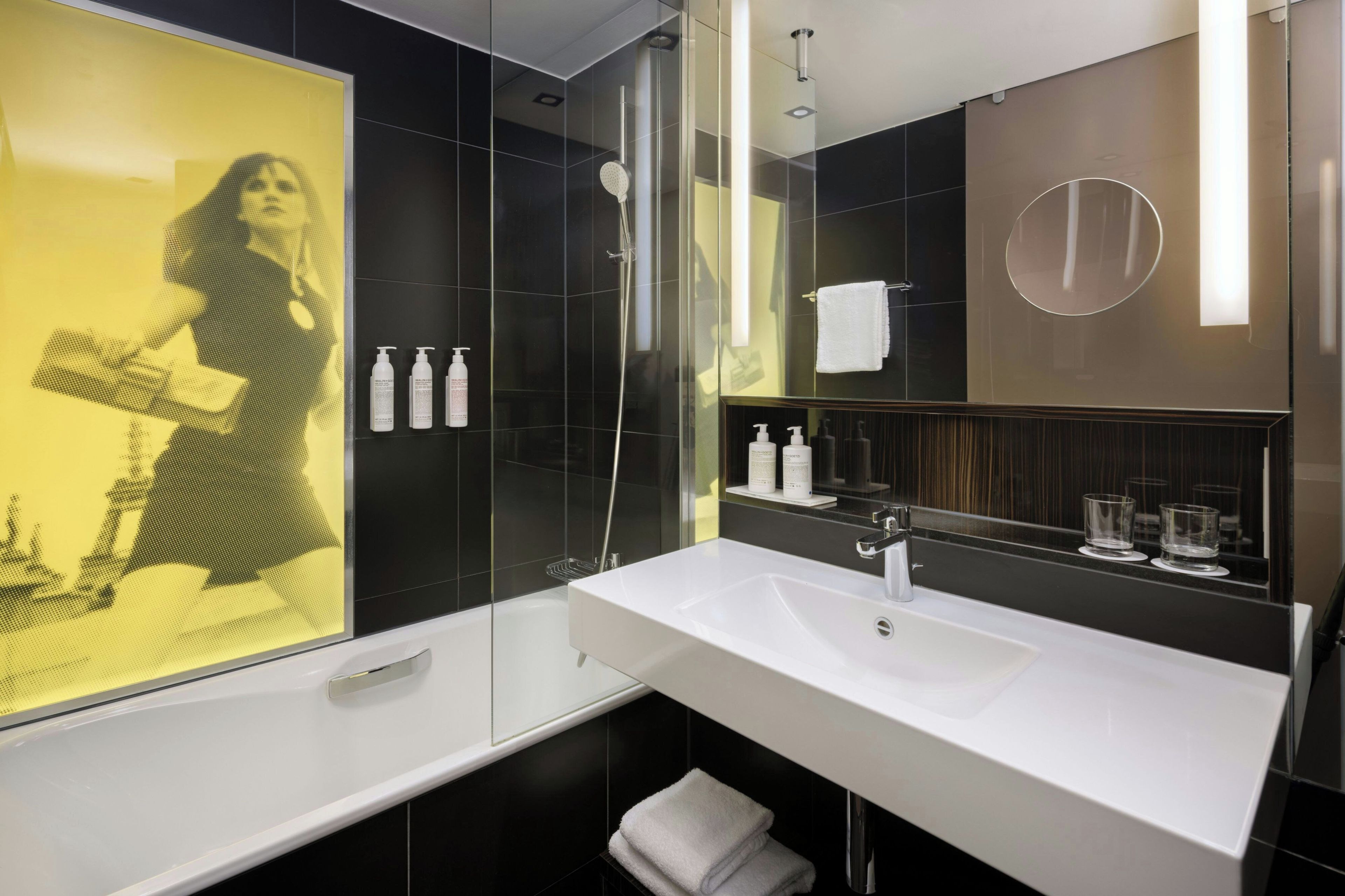 A modern bathroom with a large mirror, white sink, and black tiles.