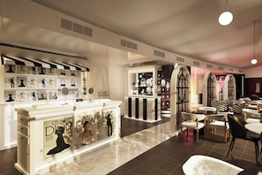 A modern interior with a central counter displaying fashion magazines, a seating area with tables and chairs, and a vanity area with mirrors and lights. - Le Méridien Paris Arc De Triomphe (Paris)