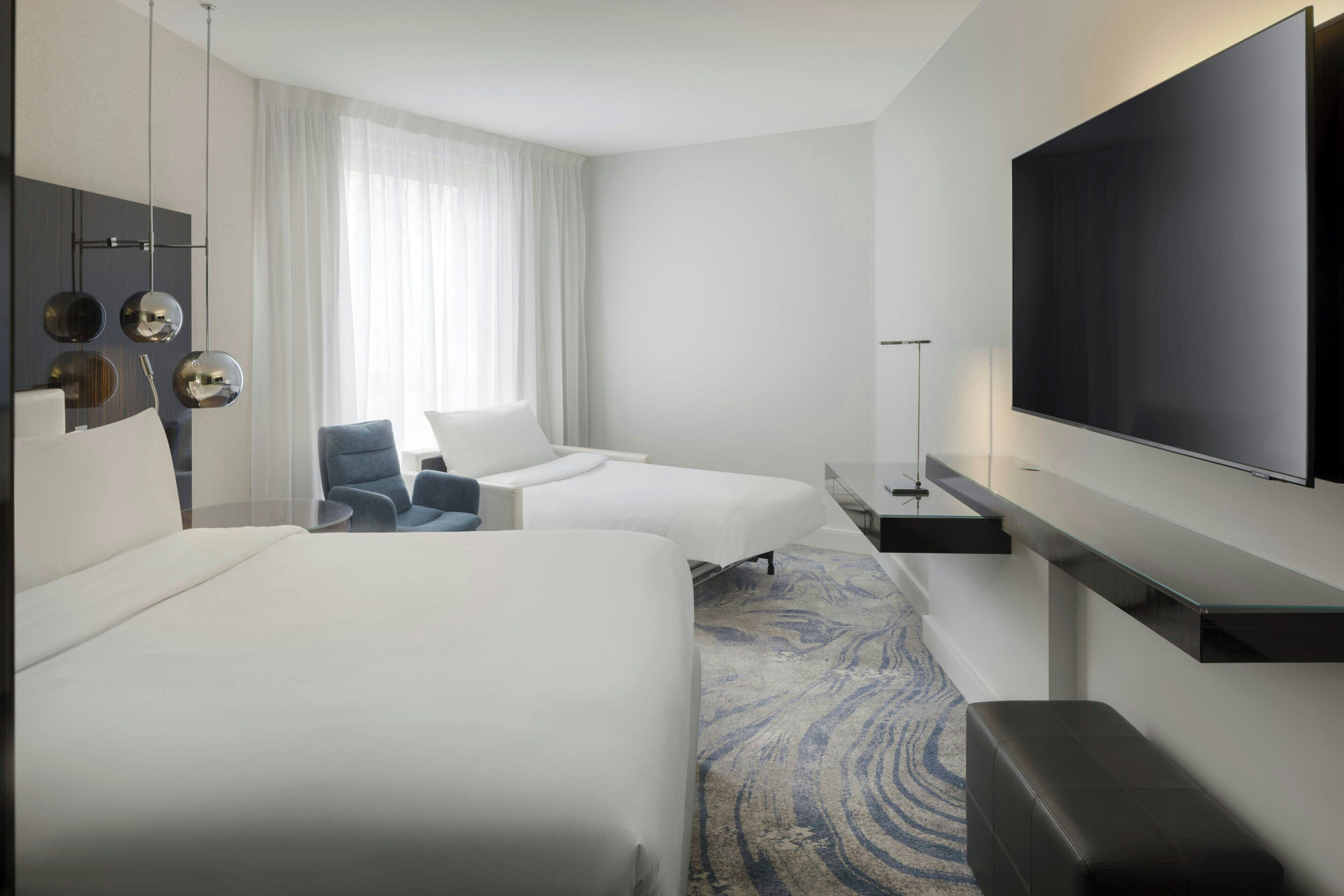Ein Hotelzimmer mit zwei Betten, einem Flachbildfernseher, einem Schreibtisch und einem Stuhl.