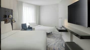 Ein Hotelzimmer mit zwei Betten, einem Flachbildfernseher, einem Schreibtisch und einem Stuhl.