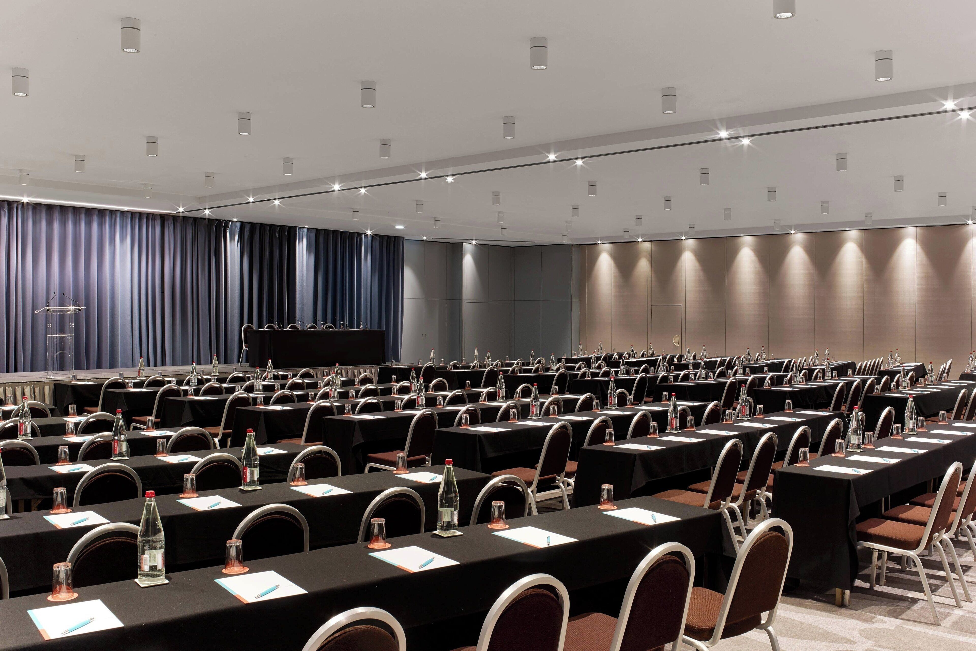 A conference room with rows of tables, chairs, and a stage.