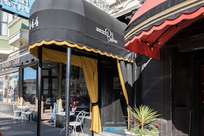 A hotel with a black awning and yellow curtains, outdoor seating, and a visible storefront with a pastry cafe. - Hotel Boheme (San Francisco)