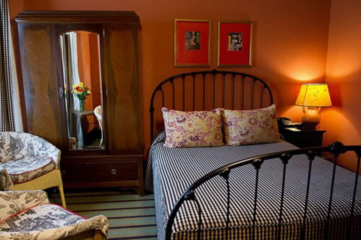 A bedroom with a bed, a chair, a wardrobe, and two framed pictures on the wall.