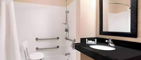 A modern bathroom with a white bathtub, a white chair, a black sink, and a large mirror.